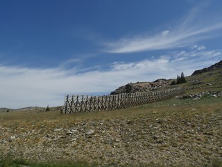 Fototapeta na wymiar Hillside view with a high wooden fence on a beautiful day in Wyoming.