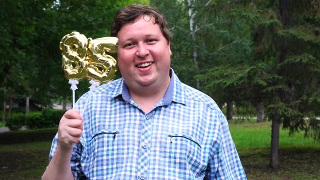 Big man holding golden balloons making the 85 number outdoor. 85th anniversary celebration party