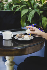 Close-up of a person's hand chocolate balls with coffee and laptop on round wooden table