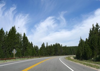 Fototapeta na wymiar Curbing road with lush forests and beautiful cloud formations in the skies at Bighorn County in Wyoming.