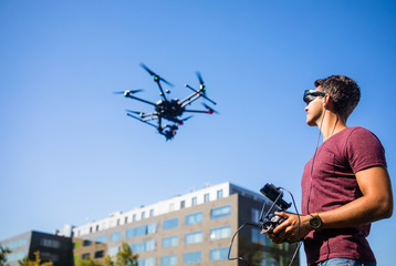 Handsome young man flying a drone outdoors using a VR/augmented reality glasses to operate the...