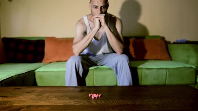 Depressed man suffering from suicidal depression want to commit suicide by overdose taking strong medicament drugs and pills pain killers sitting in his dark room selective focus moody dramatic look