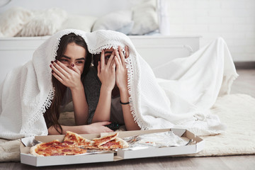 One girl is smiling, other is scared. Warm blanket. Sisters eating pizza when watching TV while...