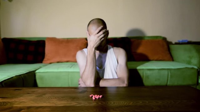 Depressed man suffering from suicidal depression want to commit suicide by overdose taking strong medicament drugs and pills pain killers sitting in his dark room selective focus moody dramatic look