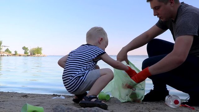 A small child collects trash on the beach. His dad points his finger where to throw garbage. Parents teach children cleanliness. Clean planet concept 