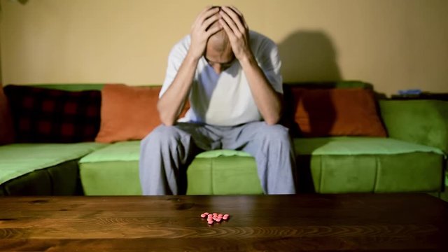 Depressed man suffering from suicidal depression want to commit suicide by overdose taking strong medicament drugs and pills pain killers sitting in his dark room selective focus moody dramatic look