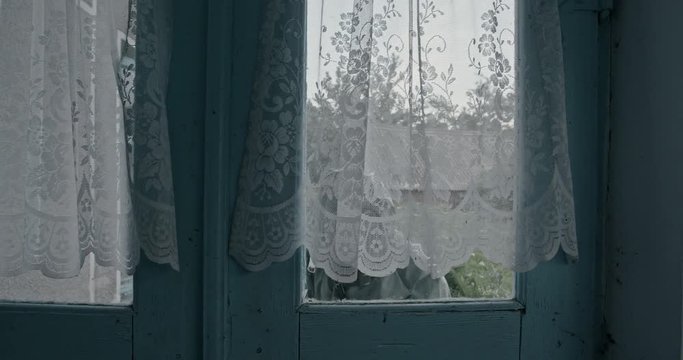 Man in a WWII Hazmat suit and gas mask approaching a curtained window from outside and trying to peer in below the fabric. RAW video record.