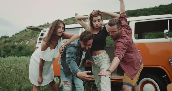 Two charismatic couples , have a great time together at the nature , taking pictures using a the phone , and standing beside a retro van.