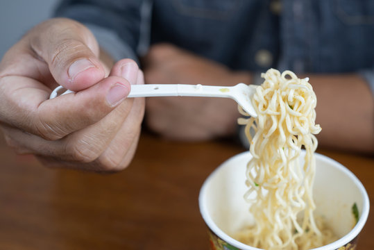 Selective focus Young man hand holding plastic fork of instant noodles, Eating Instant noodles in cup with a fork, junk food concept