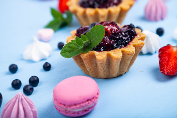 Small berry cake and ripe berries on a blue wooden background. Delicious dessert.