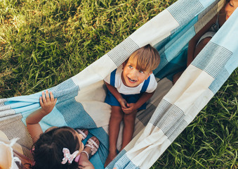 Above view image of playful children playing on the blanket together on the green grass. Happy little boy and little girls enjoying summer day in the park. Cheerful kids playing outdoors. Childhood