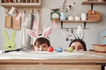 Looking fron under the table. Mother and daughter in bunny ears at easter time have some fun in the kitchen at daytime
