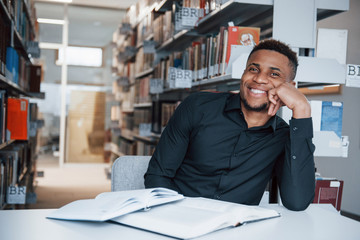 Time for the rest. African american man sitting in the library and searching for some information in the books