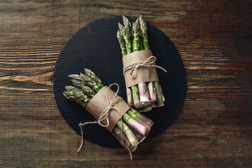 An edible, raw stems of asparagus on a wooden background.