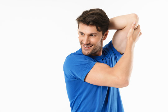 Cheerful young sports fitness man standing isolated over white wall background make stretching exercises for arms triceps.