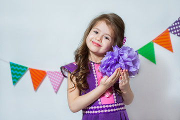 Little girl holding a paper pompon on a white background and colored garlands. Theme holiday, birthday.