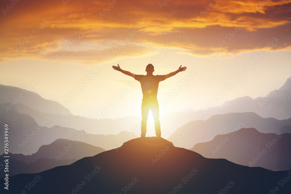 Wall mural man standing on edge of mountain feeling victorious with arms up in the air.