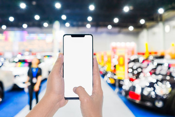 Mock up mobile phone. Hand holding mobile phone with abstract blurred cars exhibition show background image. Car shopping online, internet and social network background concept.