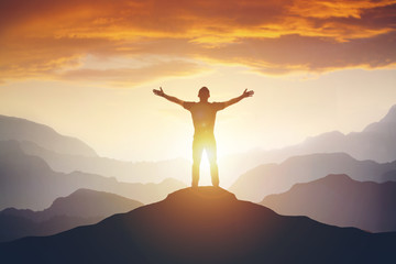Man standing on edge of mountain feeling victorious with arms up in the air. - obrazy, fototapety, plakaty