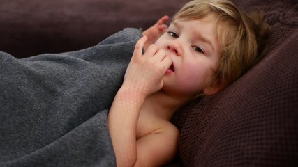 The girl pokes her finger in her nose. Pensive child