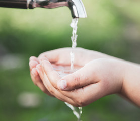 boy washes his hand under the faucet in garden