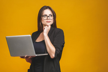 Young happy smiling woman in casual clothes holding laptop and sending email to her best friend isolated against yellow background.