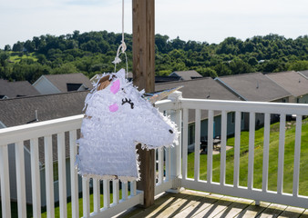 White pinata shaped like a unicorn hanging on the deck of modern home in USA for childs party