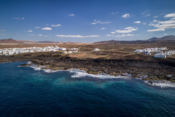 Drone view of a spanish island, volcano beach,  blue sky, clouds , white houses on the coast, pastel tons, Lanzarote. 
