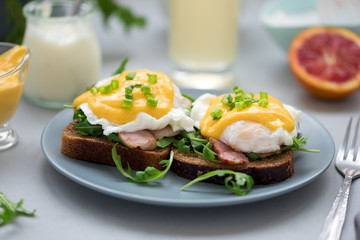 Close up eggs Benedict with arugula, bacon and hollandaise sauce on gray wooden background. Soft focus. Healthy eating concept