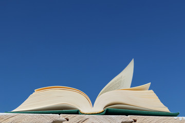 An open green book lies on a background of blue sky. The concept of summer reading, outdoor recreation with a book. Bright sunny day. Copy space.