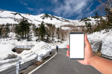 hand hold mobile phone with a road of snow wall japan alps mountain, Japan.