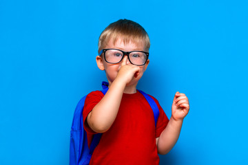 small smiling schoolboy on blue background in glasses toutch his glasses. back to school, preschool kid
