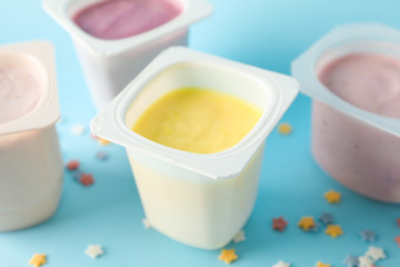 Fototapeta na wymiar Plastic cups with yogurt and small stars on color background