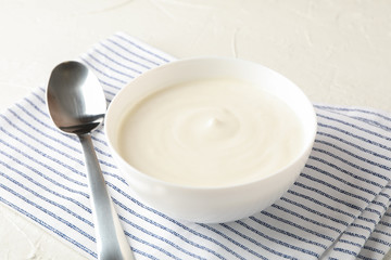 Bowl of sour cream yogurt, spoon and towel on white cement background