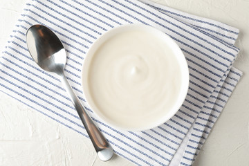 Bowl of sour cream yogurt, spoon and towel on white cement background
