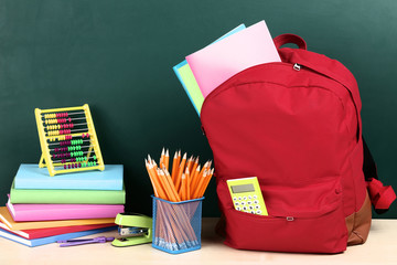 Backpack with school supplies on green background