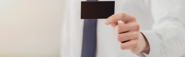 cropped view of businessman showing at camera empty black business card, panoramic shot