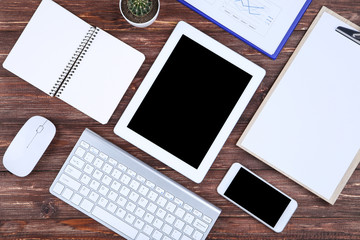 Tablet, keyboard computer with smartphone, mouse and notepad on brown wooden table