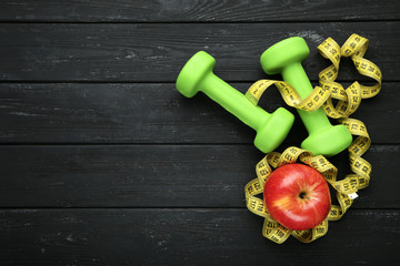 Dumbbells and measuring tape and apple on black wooden table