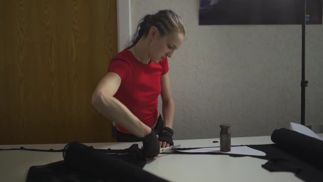 Cyber punk fashion designer at work in her studio cutting pattern - Caucasian white woman wearing red t-shirt and black gloves with scissors hanging over her chest
