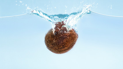 Ripe coconut falling in clear water with splash
