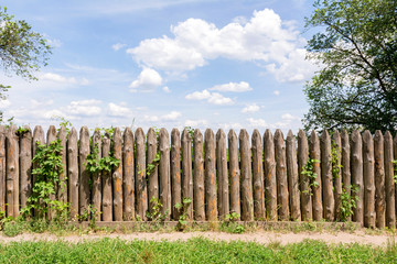 Old fence of logs. Palisade against the blue sky