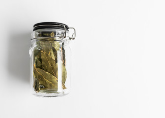 glass jar with dry bay leafs on white background