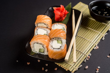 Close up sushi rolls in a black plate on dark background