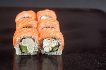 Close up sushi rolls in a black plate on dark background