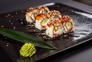 Sushi california roll with sauce and sesame on black plate