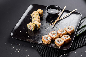Sushi rolls on black plate with bamboo leaves and chopsticks
