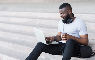 Happy african guy having rest in the city and using Internet