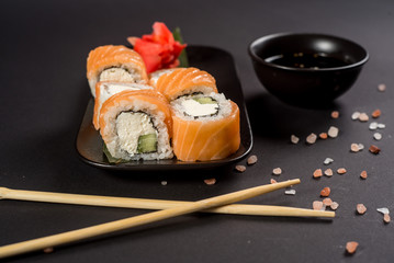 Close up sushi rolls in a black plate on dark background
