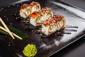 Sushi california roll with sauce and sesame on black plate